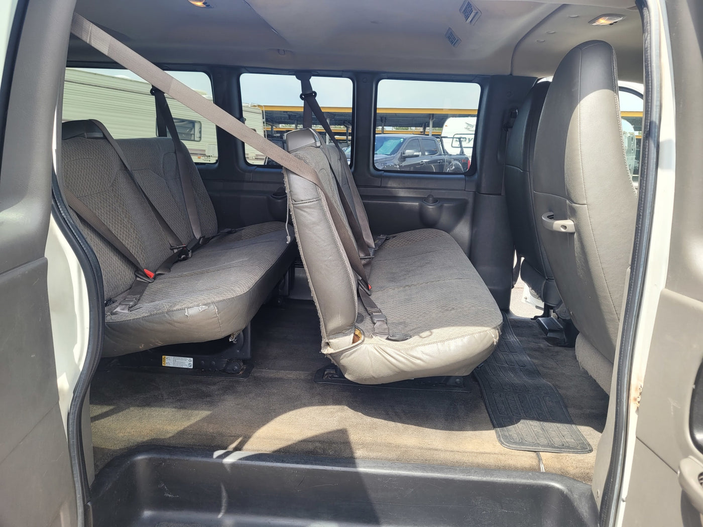 Interior of a passenger van, showing two rows of grey seats with seatbelts. An RV is outside, suitable for rv rental. — photo 11