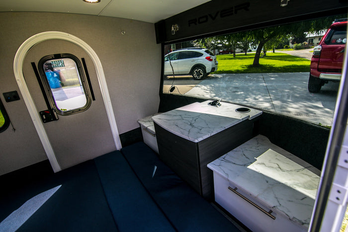 Explore this compact **RV rental** interior with a cozy sleeping area, marble-top dining table, and scenic view from the large window.