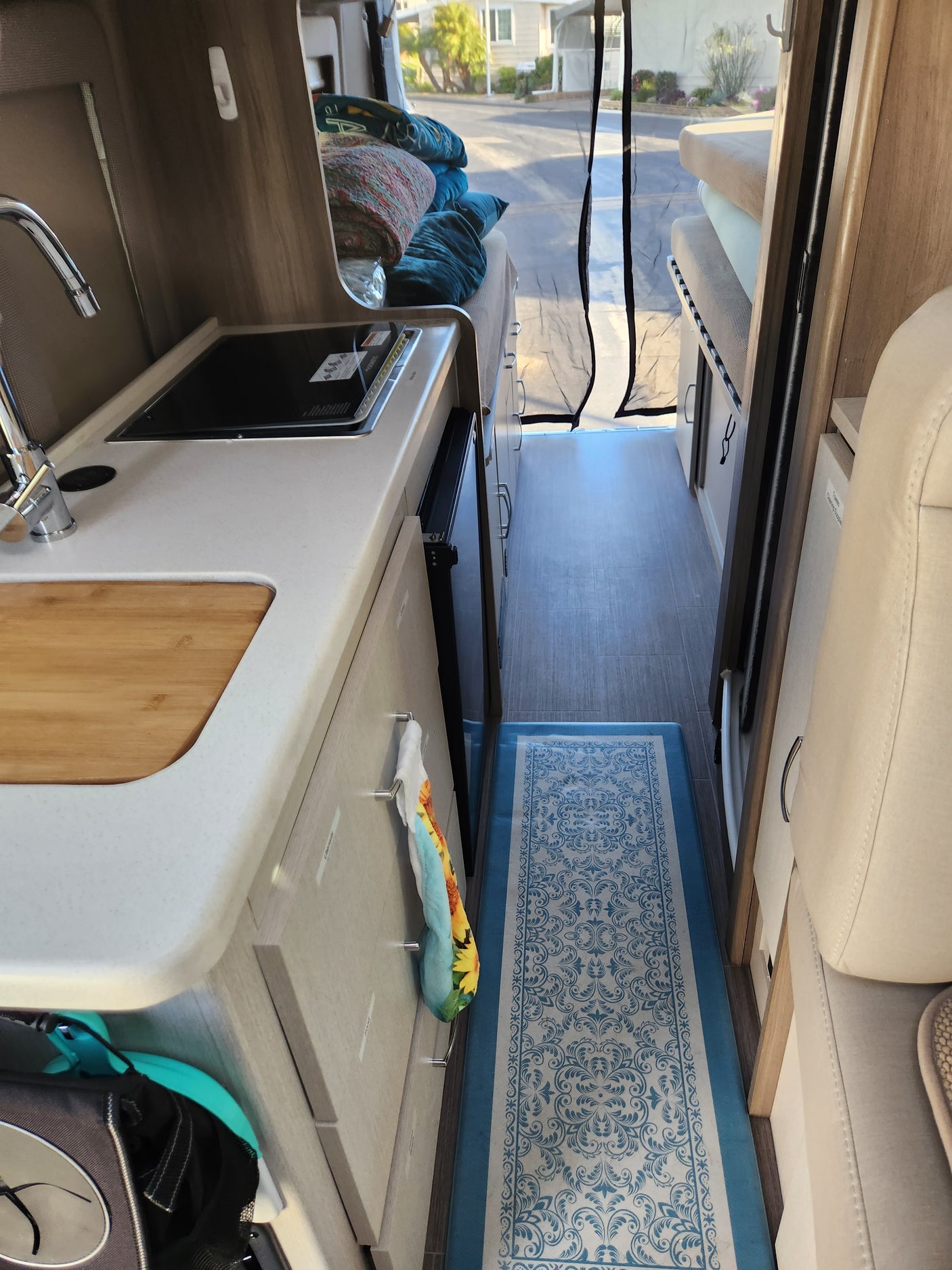 Inside a bright rv rental, featuring a compact kitchen with sink, microwave, and a cozy sleeping area.