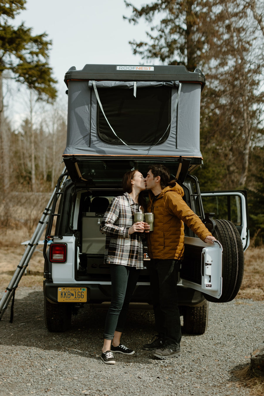 A couple kisses by their white Jeep with a Roofnest rooftop tent. Perfect RV rental for memorable outdoor adventures in Alaska!
