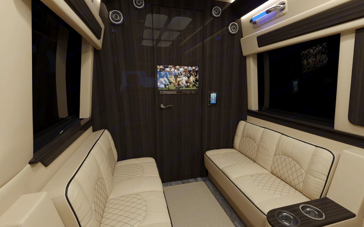 Luxurious RV rental interior with facing cream seats, dark wood walls, and a TV entertainment system. Travel in comfort and style.