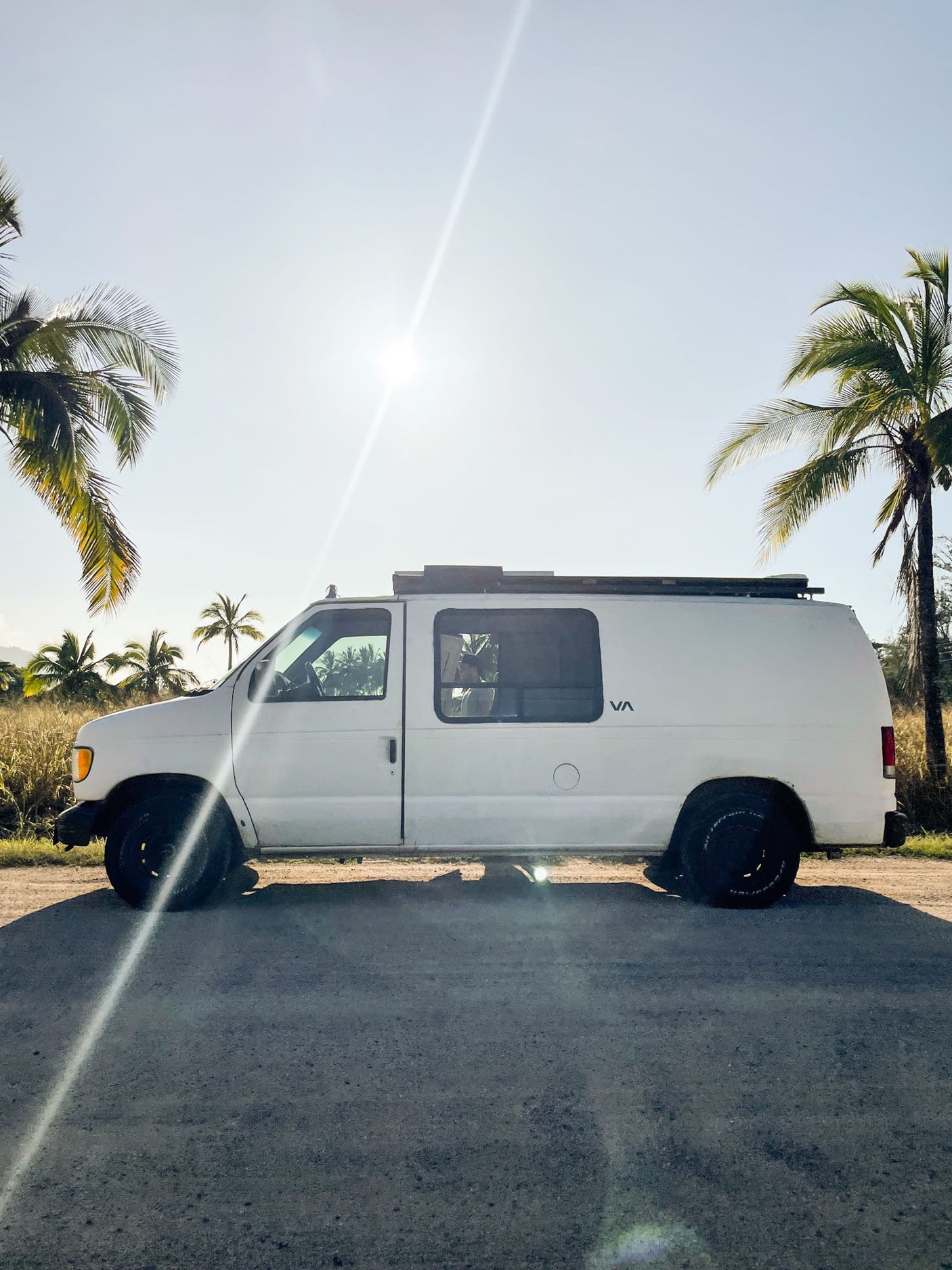 White RV rental van parked on a sunny road with palm trees. Perfect for a tropical adventure.|Step inside this RV rental!|An Asian woman works on her laptop in a bright