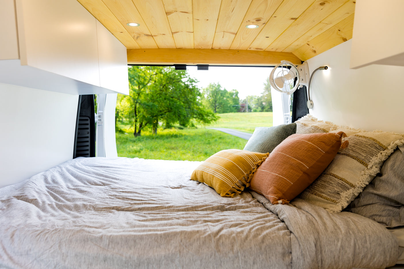 Relax in this RV rental bed! Features colorful pillows, wooden ceiling, and a stunning green view from the open back.