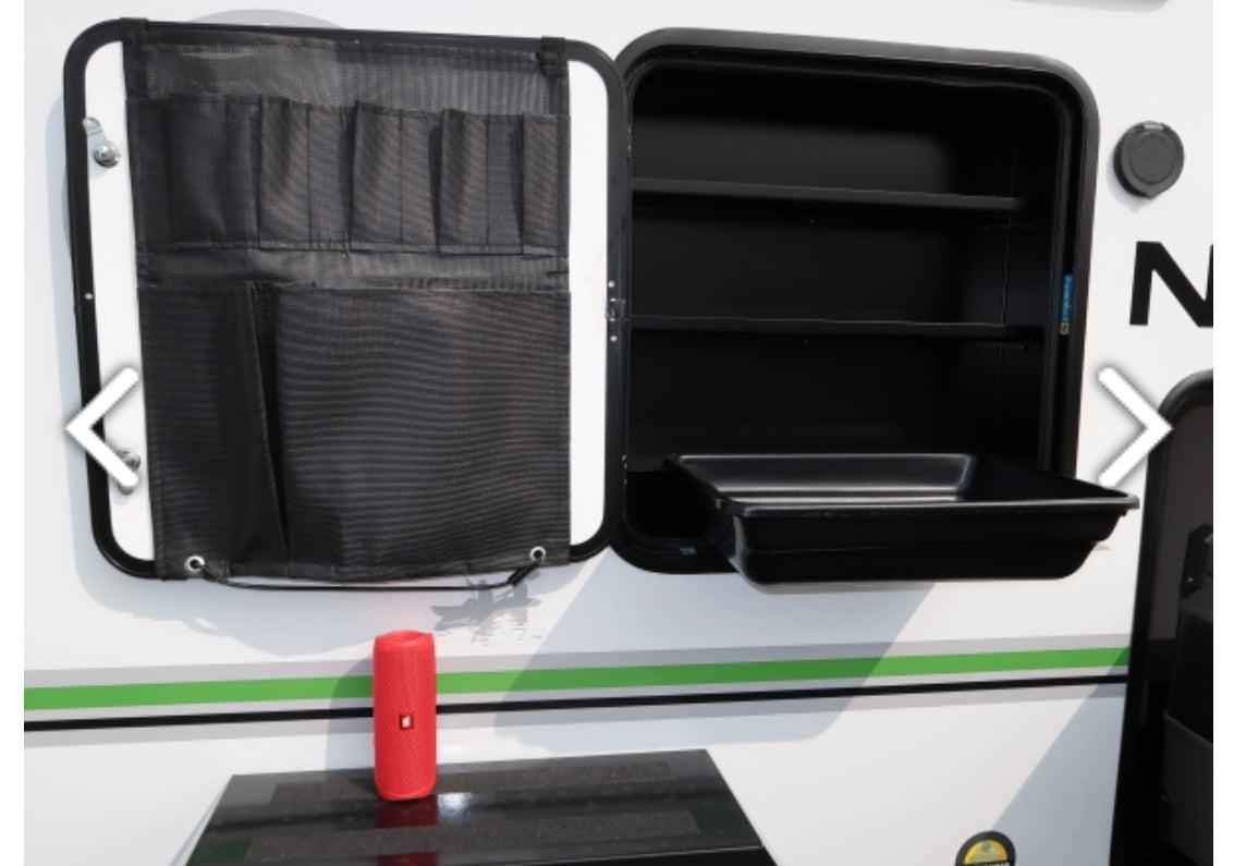 Exterior RV rental storage: open compartment with shelves, pull-out tray, & mesh door organizer.