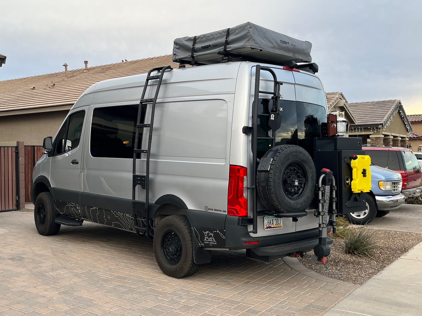 This custom Sprinter adventure van, perfect for an rv rental, features a roof tent, ladder, and rear utility setup.