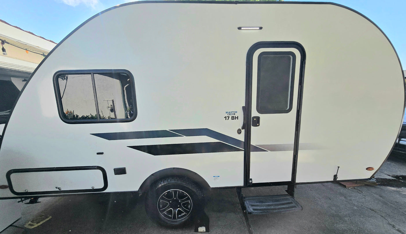 White Braxton Creek 17 BH travel trailer, perfect for an RV rental. Compact design with black graphics, side window, and entrance.