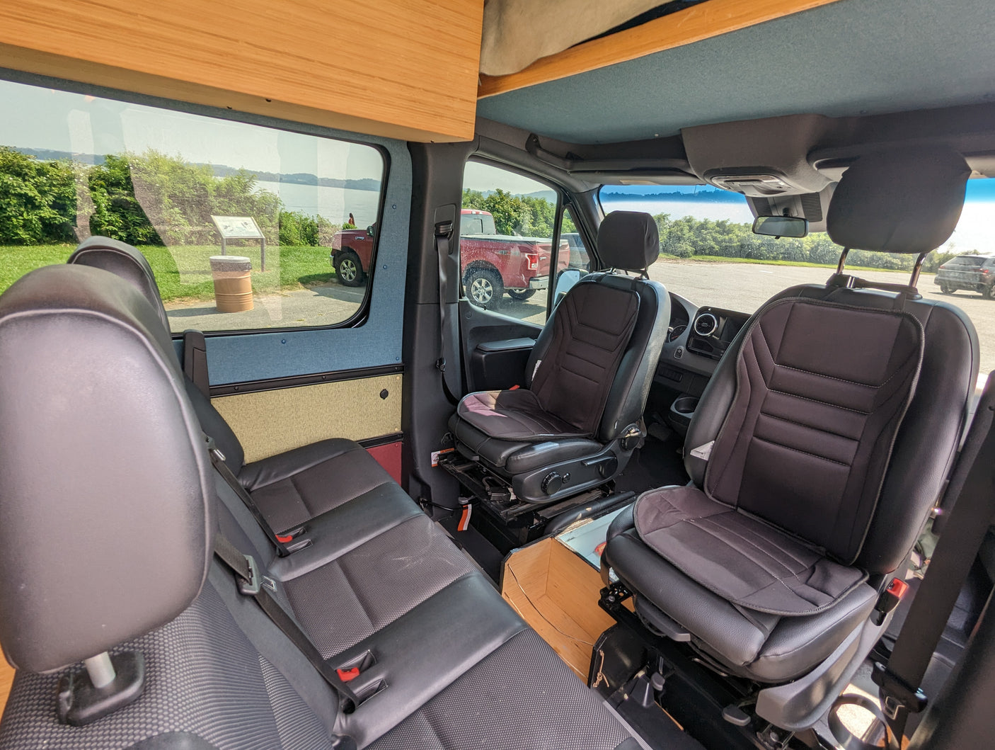 RV rental interior: View from inside a custom van, featuring black seats, wooden cabinets, and a scenic outdoor view.