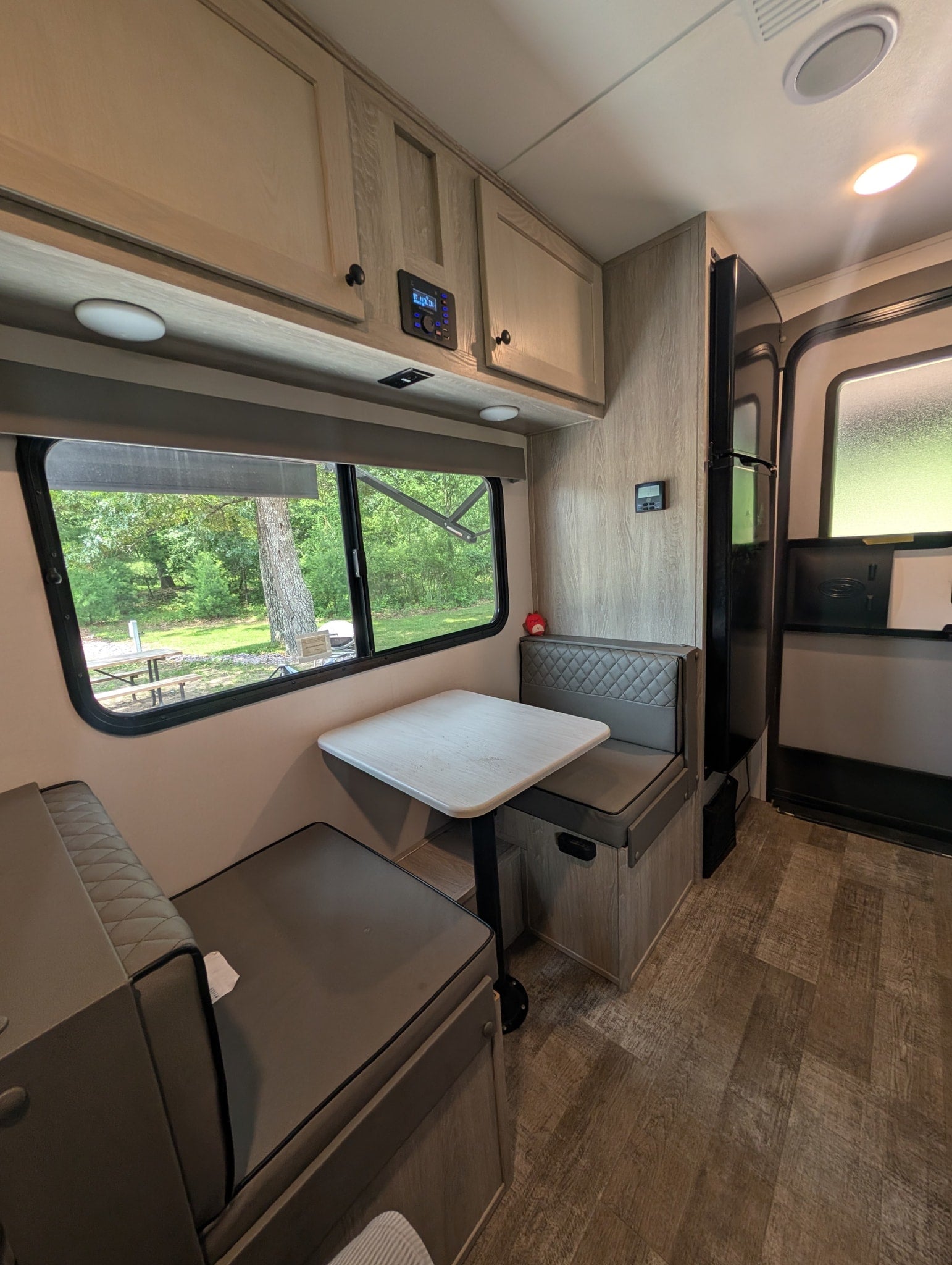 Inside this rv rental, a bright dining area with cushioned benches, a table, and a window revealing a green forest view.