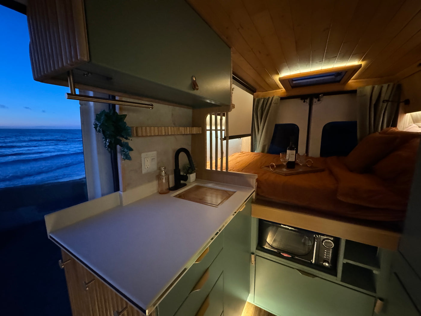 Cozy rv rental interior featuring a kitchen, microwave, comfy bed, and a serene ocean view from the window.