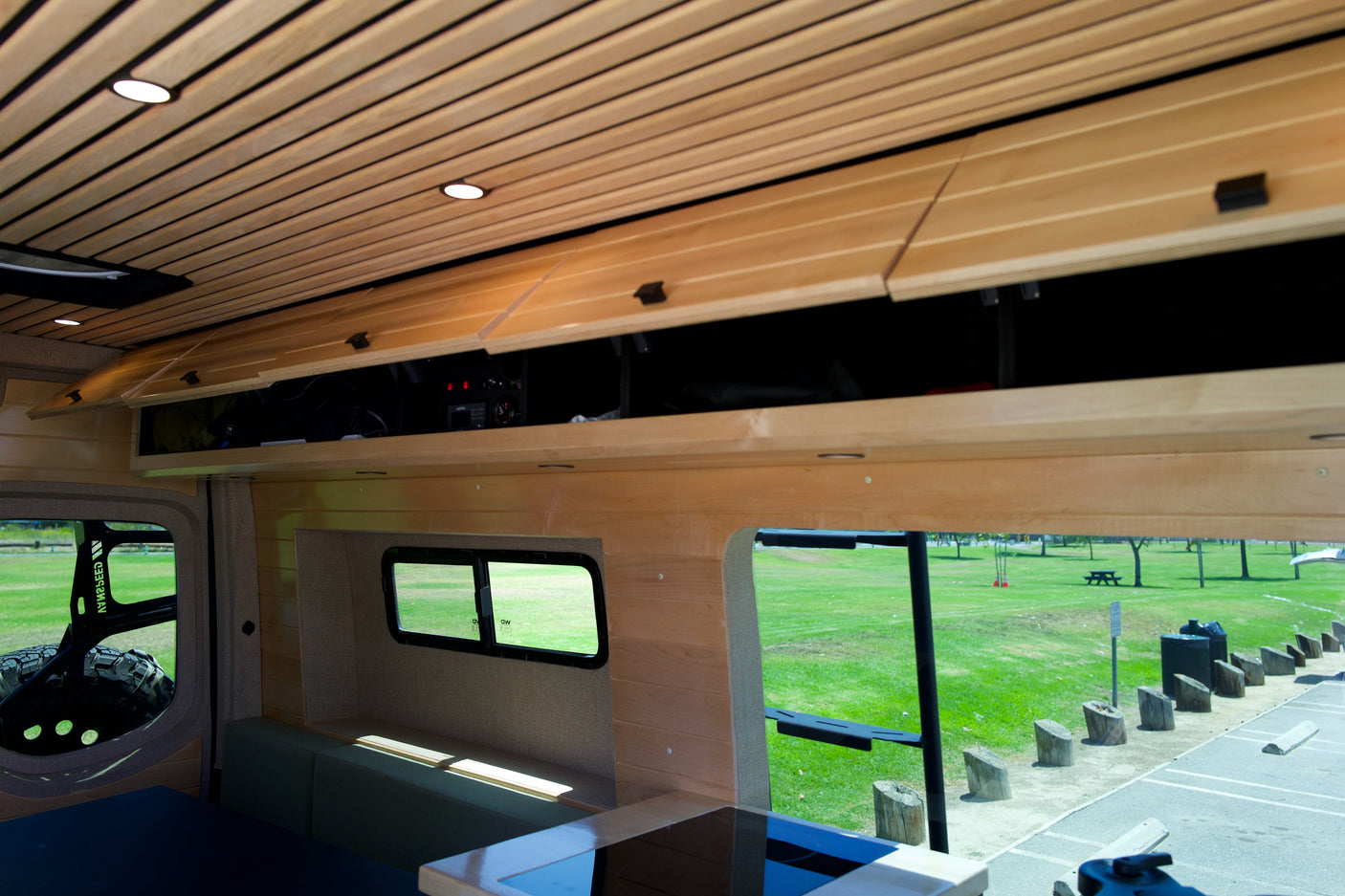 Experience this RV rental's cozy wood interior, featuring overhead storage, comfortable seating, and scenic park views through large windows.