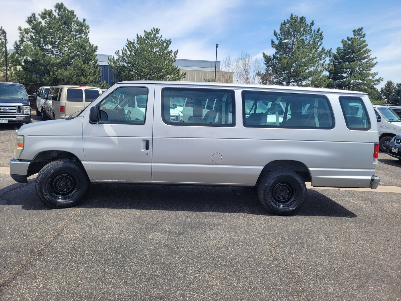 Side view of a silver multi-passenger van, seen in a parking lot. This type is often used for group travel or as an RV rental.