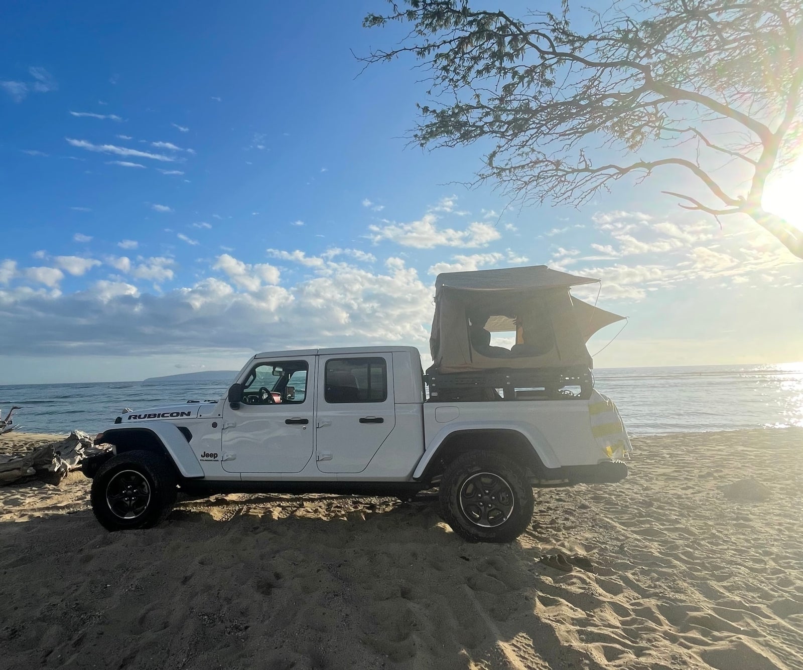 White Jeep Gladiator with rooftop tent on a sandy beach at sunrise, ideal for an RV rental adventure by the ocean.