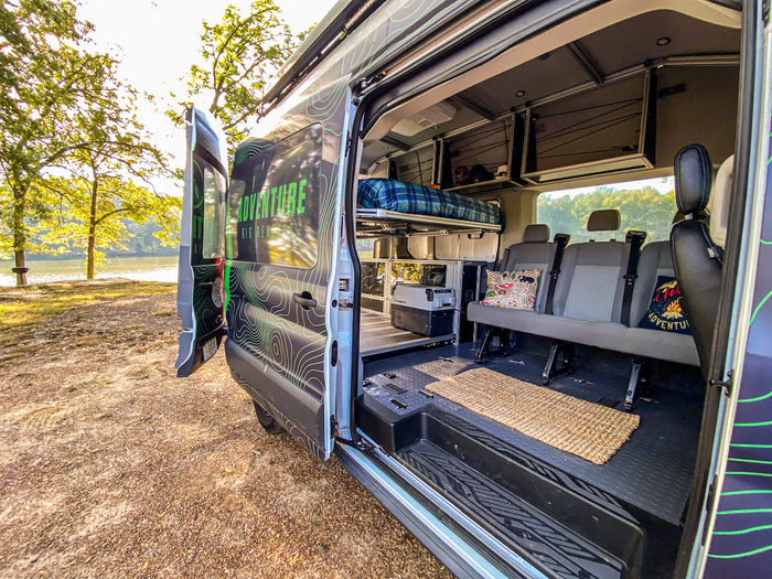 with a person by a fire pit & chairs at sunset.|This customized camper van offers comfortable mobile living