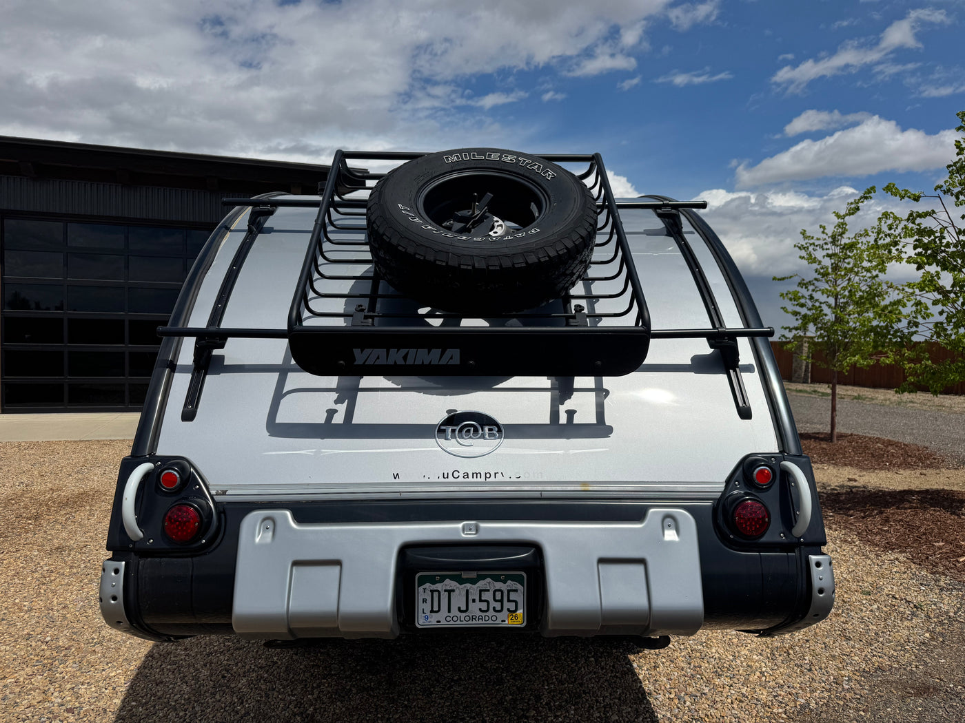 Rear view of a T@B teardrop RV rental, featuring a silver exterior, a Yakima roof rack, and a mounted spare tire, ready for camping. — photo 8