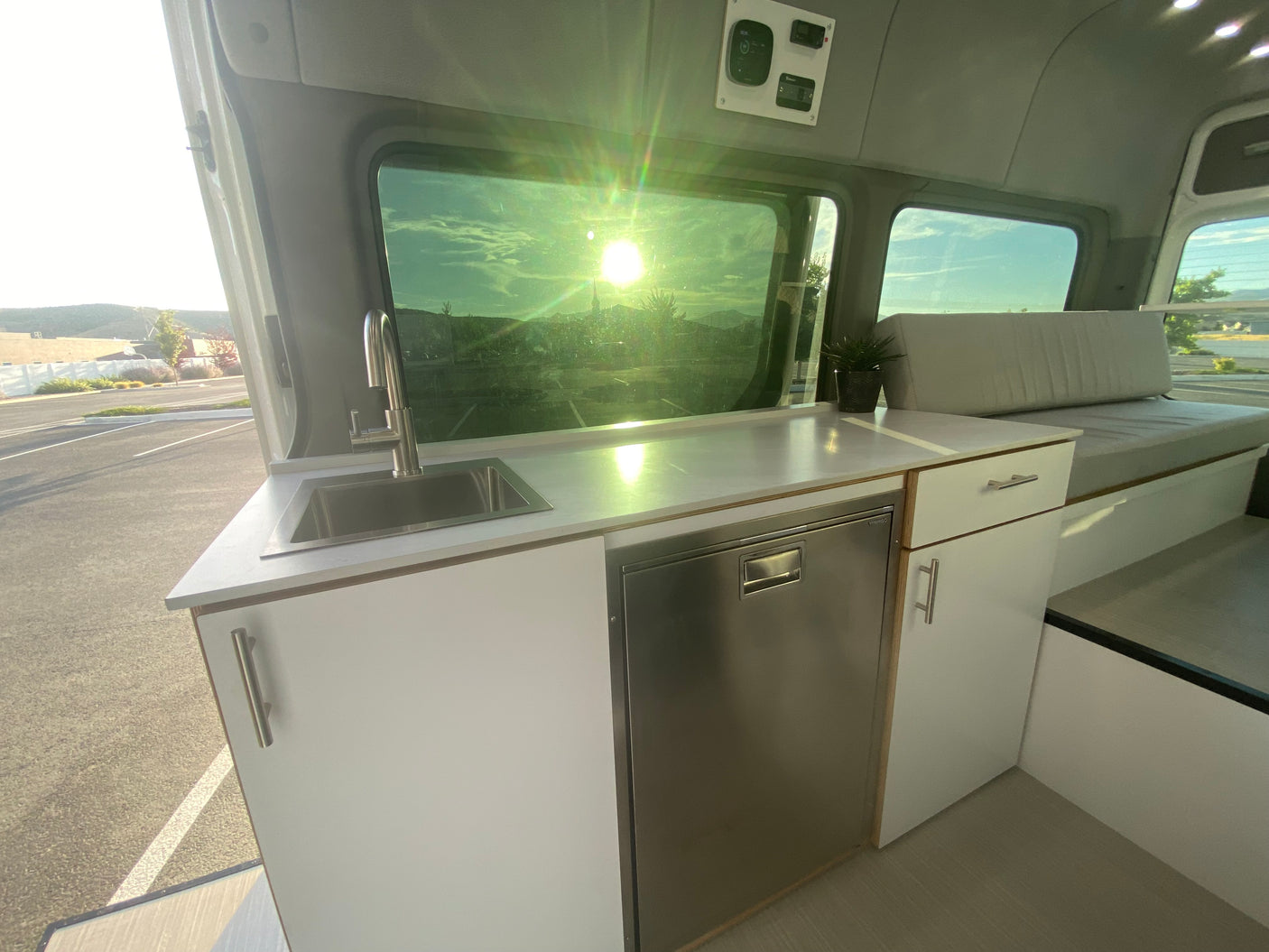 Clean RV rental kitchen & lounge area with sink, built-in fridge, and comfy bench under bright sunlight.