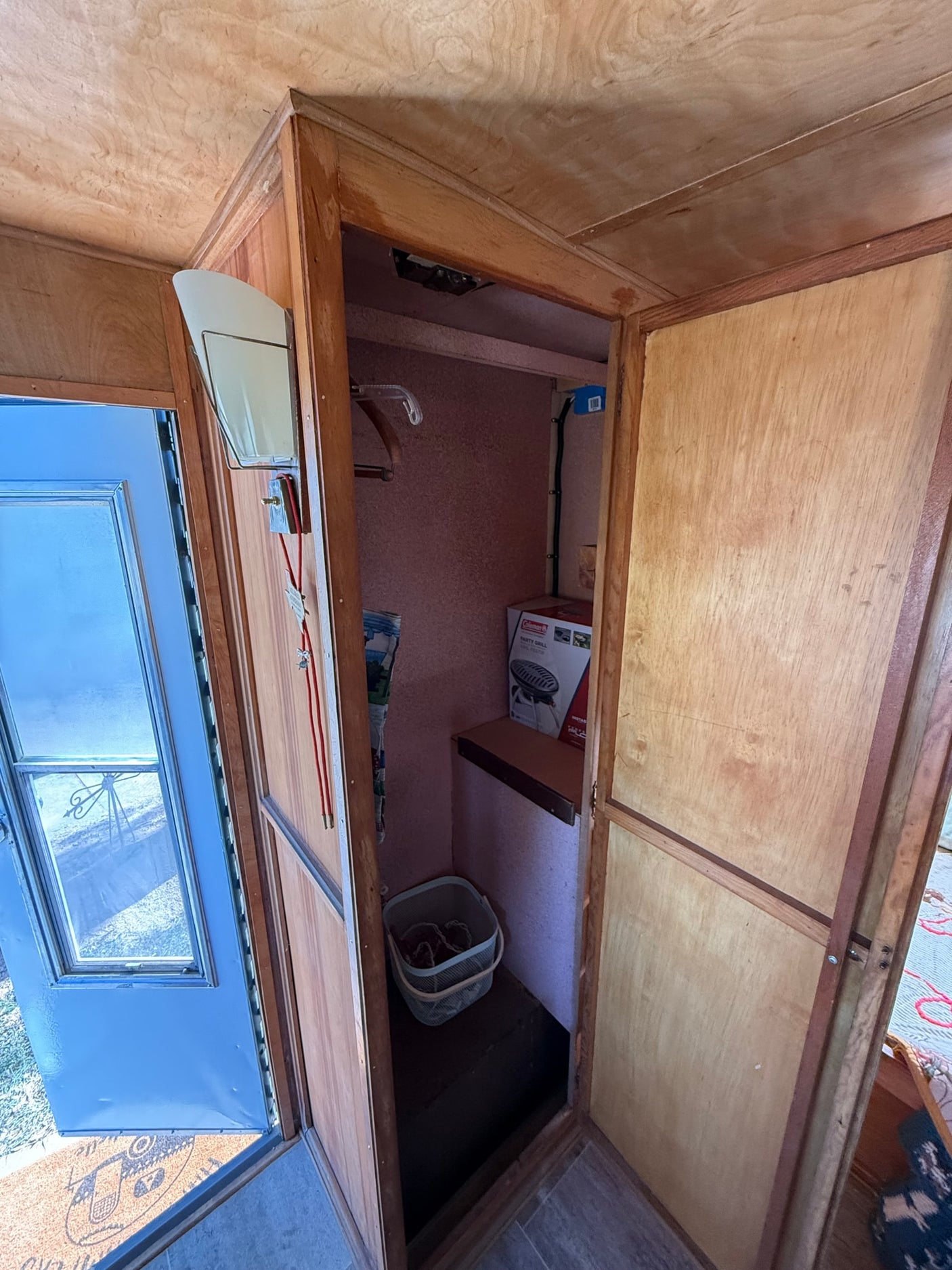Cozy RV rental interior with wooden entryway and open closet: shelf, grill box, and storage basket visible.