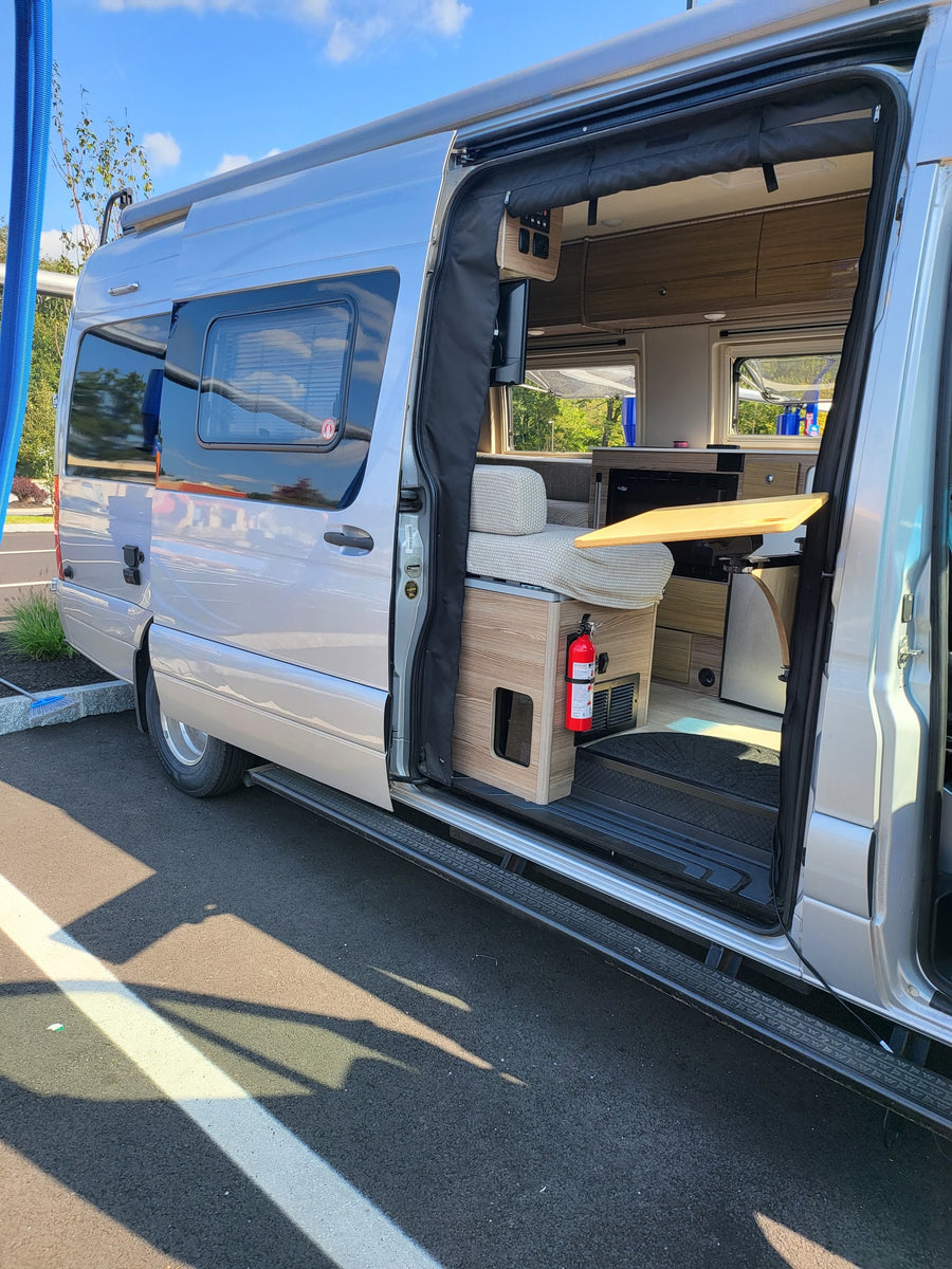 Explore this sleek silver RV rental! The open side door reveals a well-equipped interior with seating & a table.