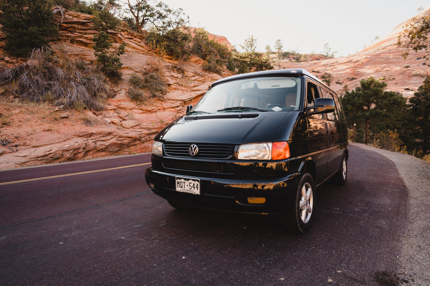Black VW campervan, ready for adventure! This RV rental is parked on a scenic road beside red rock canyons and trees.