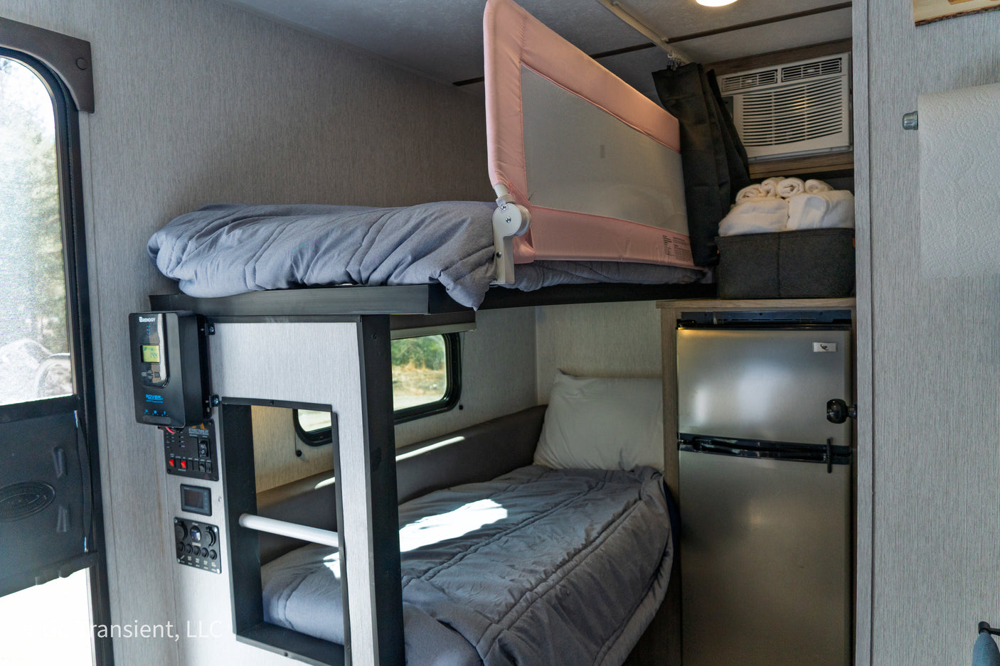 RV rental interior featuring cozy bunk beds with a child safety rail, a compact fridge, & controls. Compact living space.