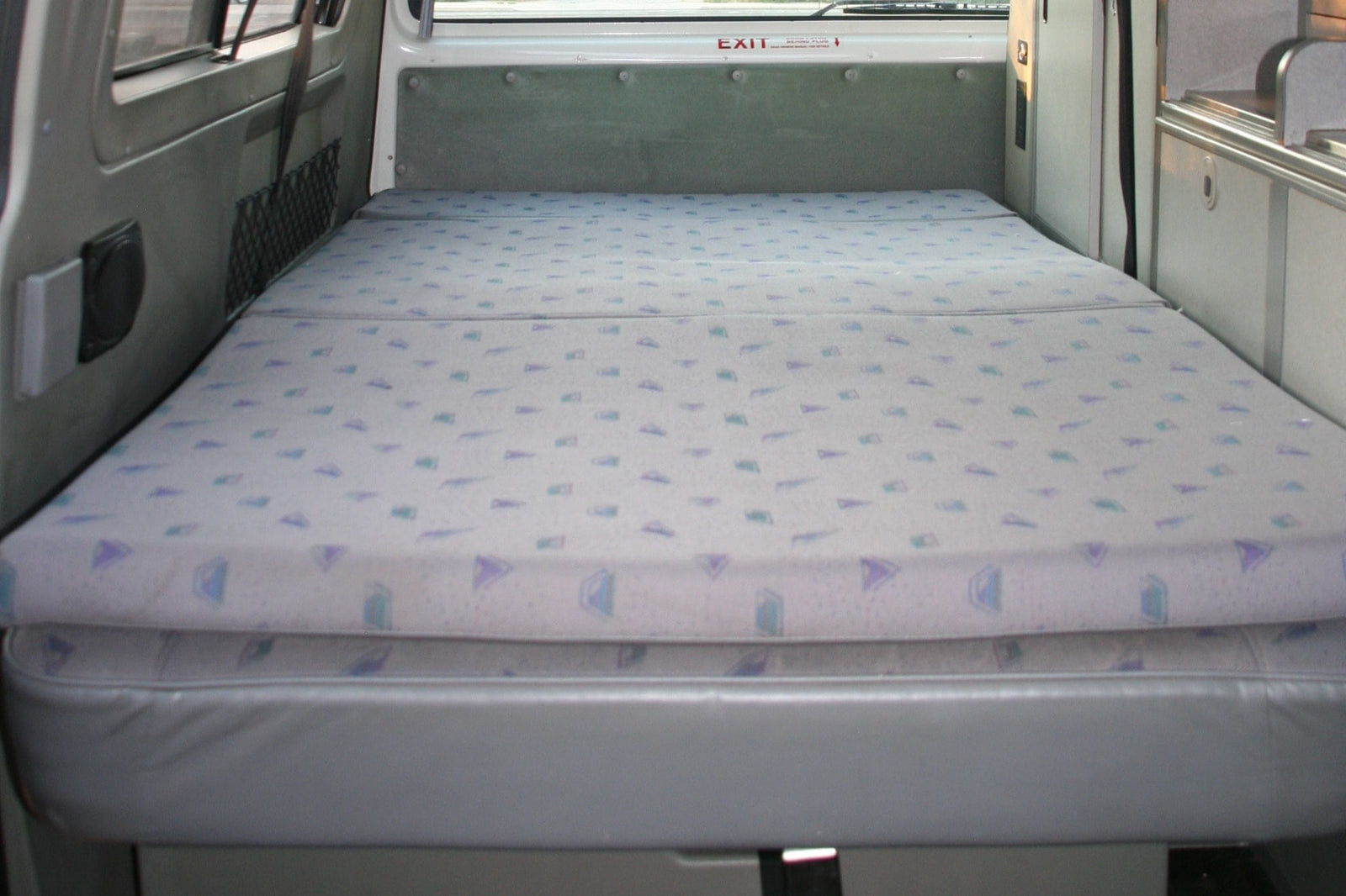 RV rental interior featuring a neatly made bed with patterned cushions on a grey base, ideal for compact travel.