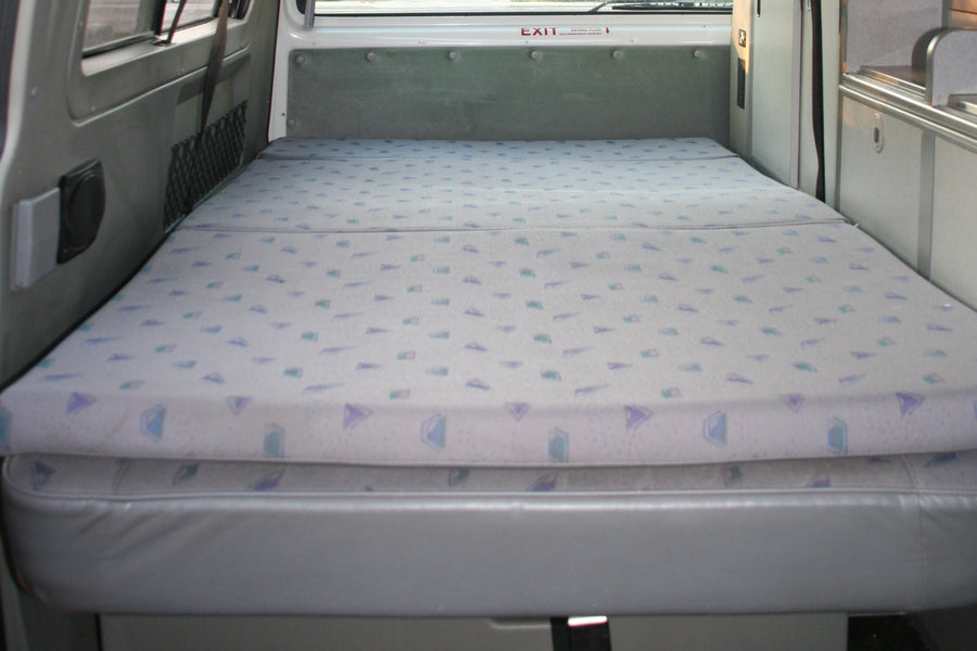 RV rental interior featuring a neatly made bed with patterned cushions on a grey base, ideal for compact travel.