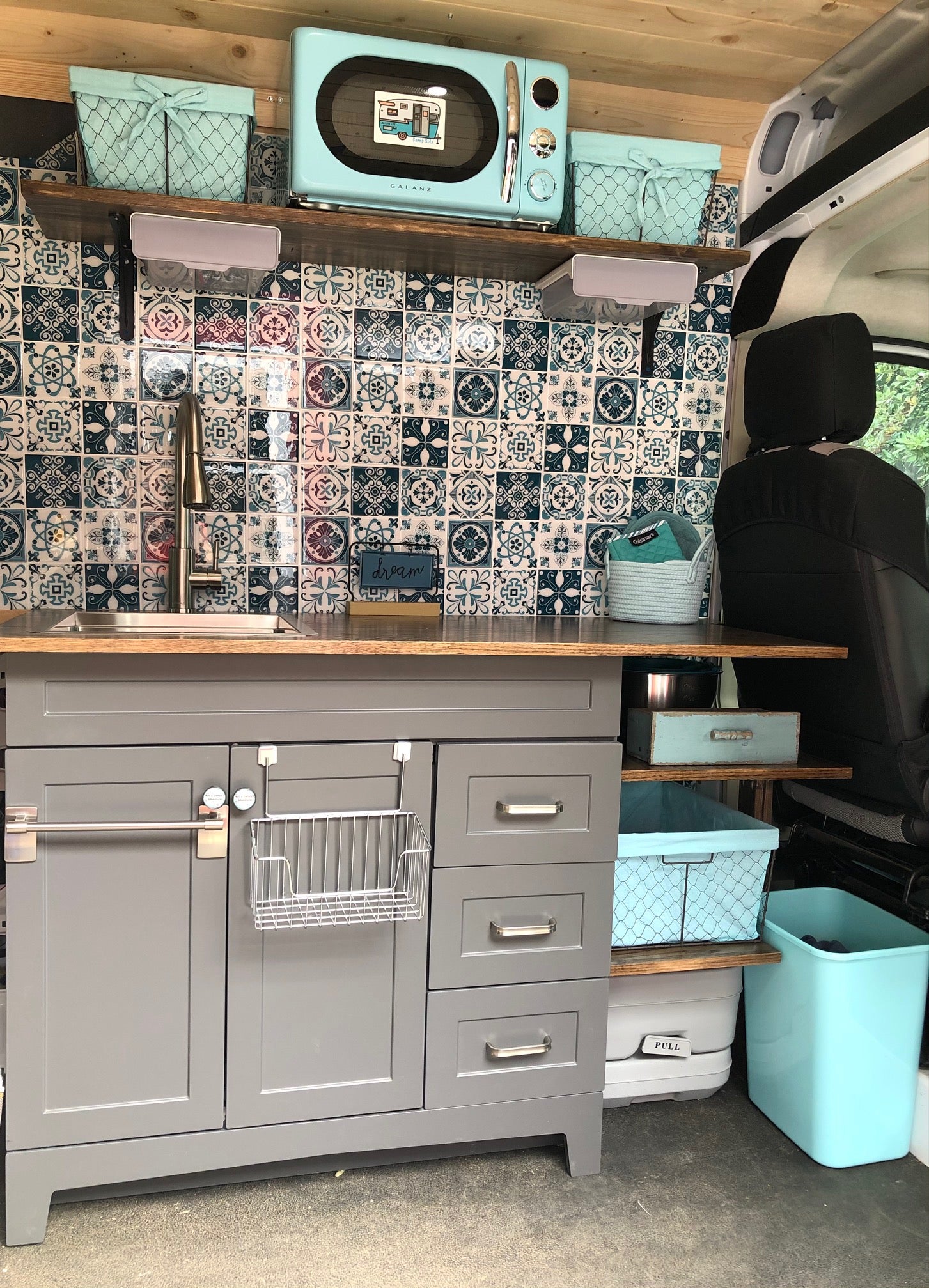 This RV rental features a bright, organized galley kitchen. Gray cabinets, a sink, microwave, and teal accents with efficient storage.