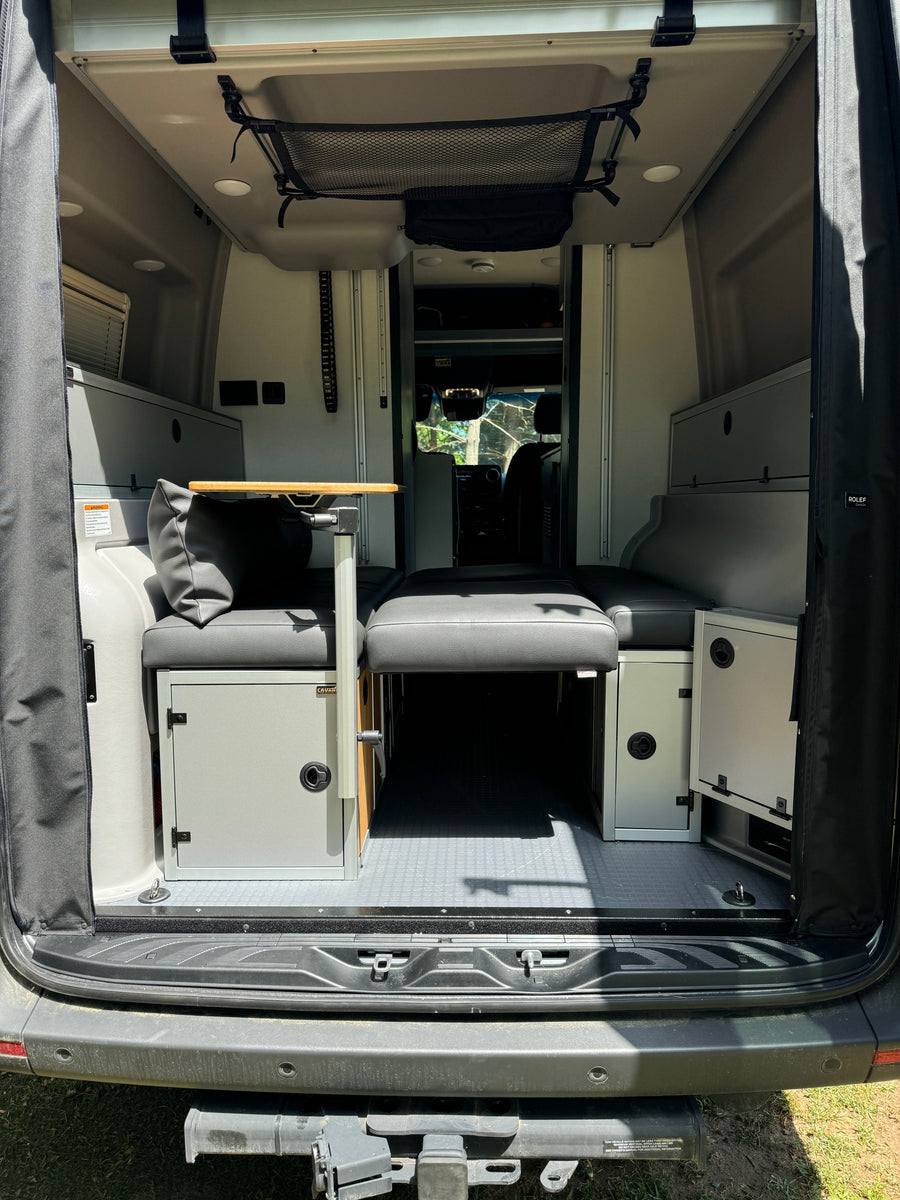 Inside this RV rental: a flexible interior with modular seating, a convertible bed, storage cabinets, table, and overhead net.