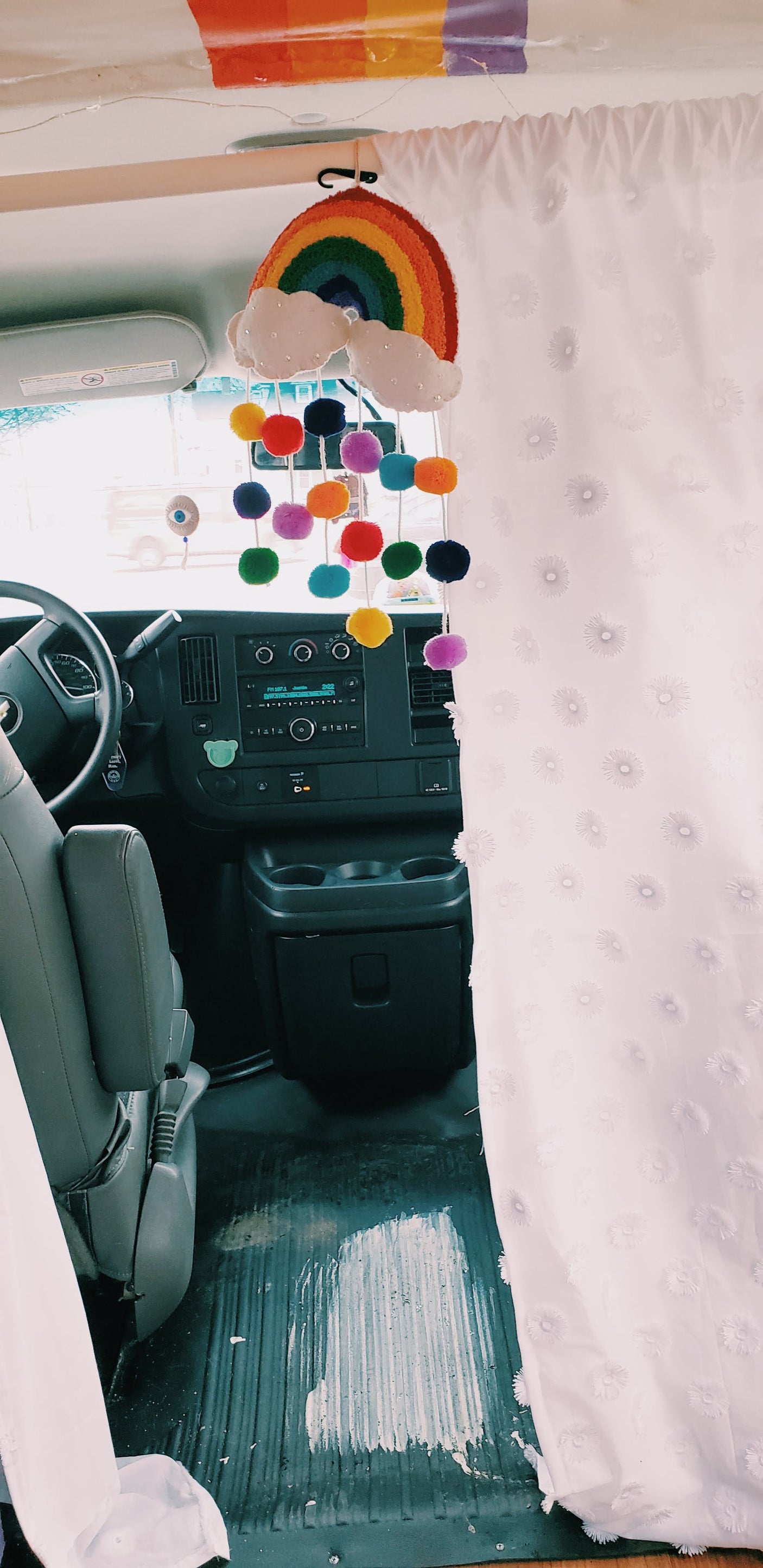 Rainbow mobile and colorful curtain adorn this cozy RV rental interior, showing the driver's area and custom decor.