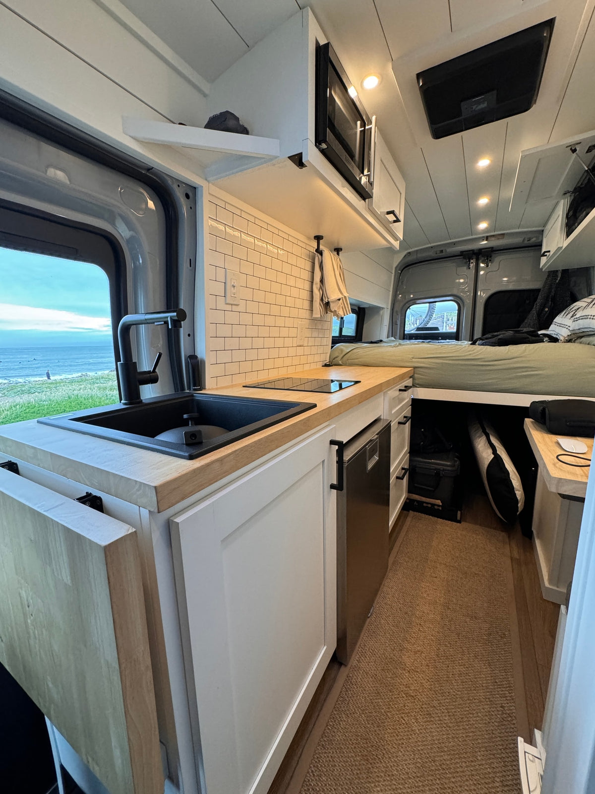 This RV rental boasts a modern kitchen, comfy bed, & ocean views. Compact, bright interior perfect for van life adventures. — photo 4