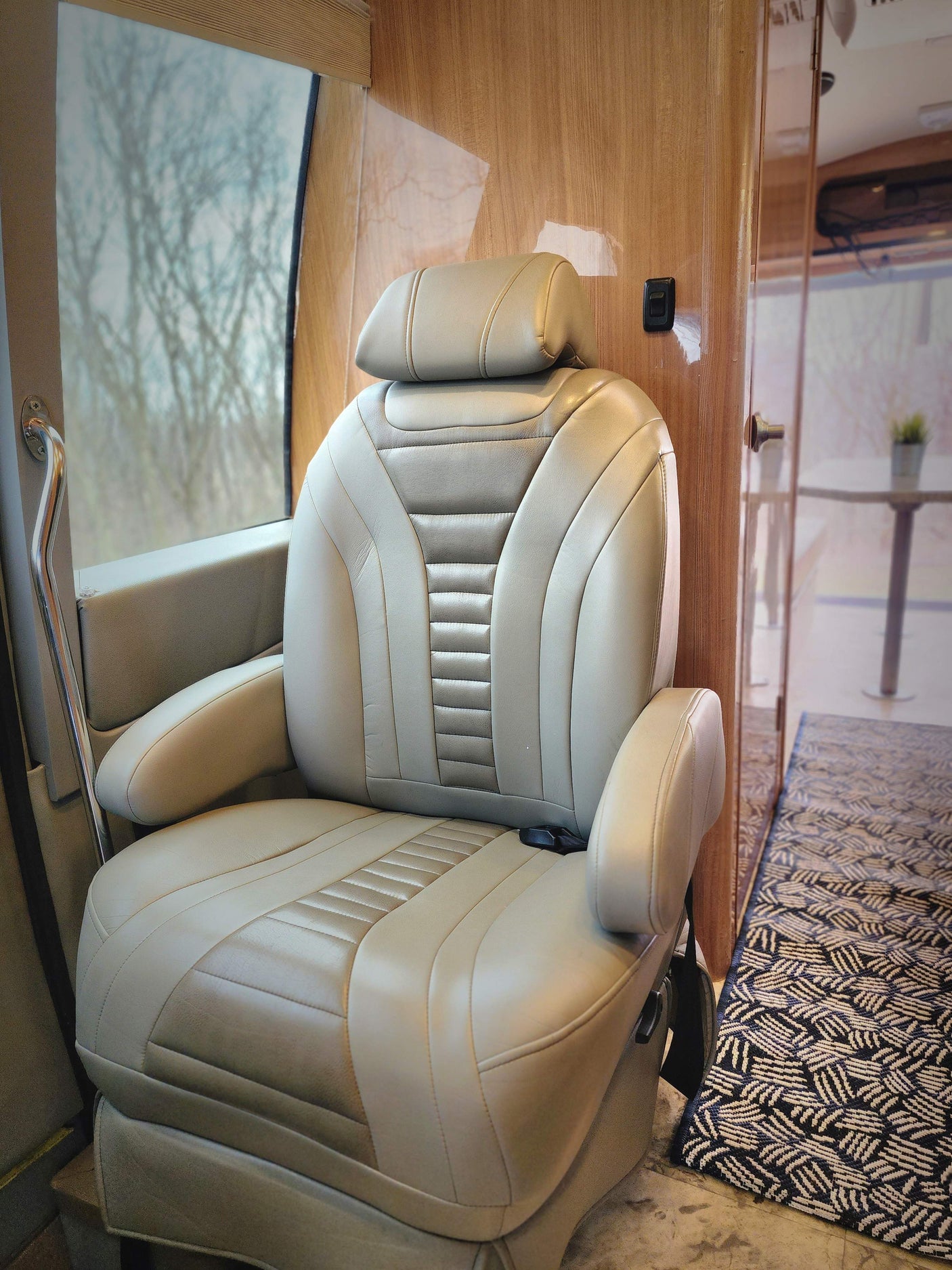 Plush captain's chair in a spacious RV rental. Features light leather, wood paneling, and a window view of trees.