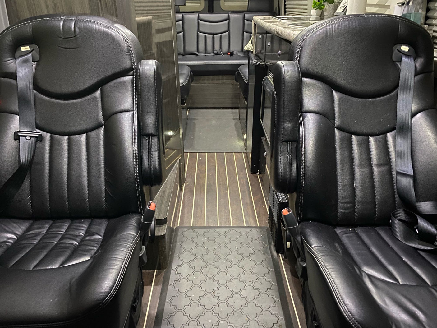 This rv rental features a luxurious van interior with two comfortable black leather captain's chairs, leading to a rear lounge area.