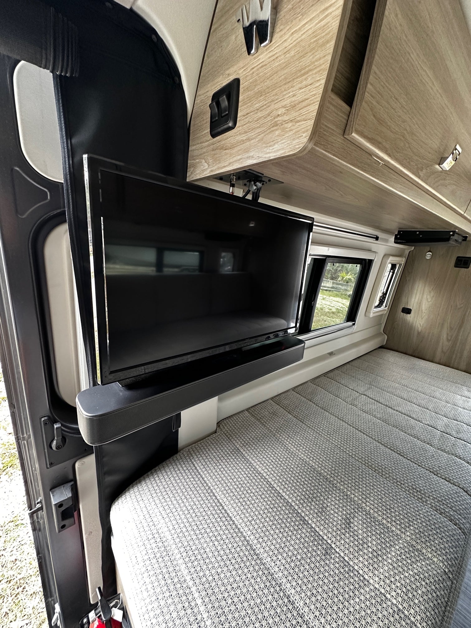 RV rental interior: Mounted TV, patterned bed, and wood storage cabinets in a camper van.