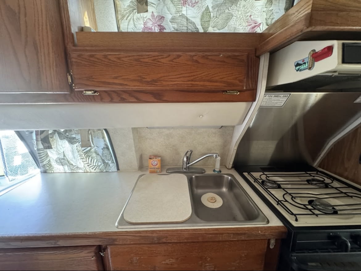 Experience this rv rental's compact kitchen, featuring a sink, stove, and oven set in warm wood cabinetry for your journey. — photo 18