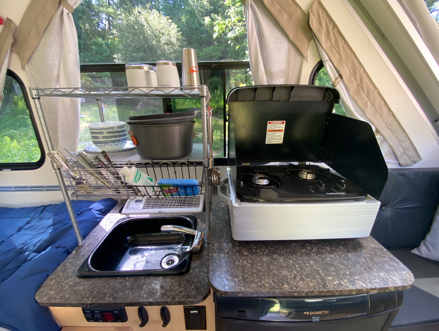 Inside an RV rental A-frame camper: organized kitchen featuring a sink, stove, and shelving for camping essentials.