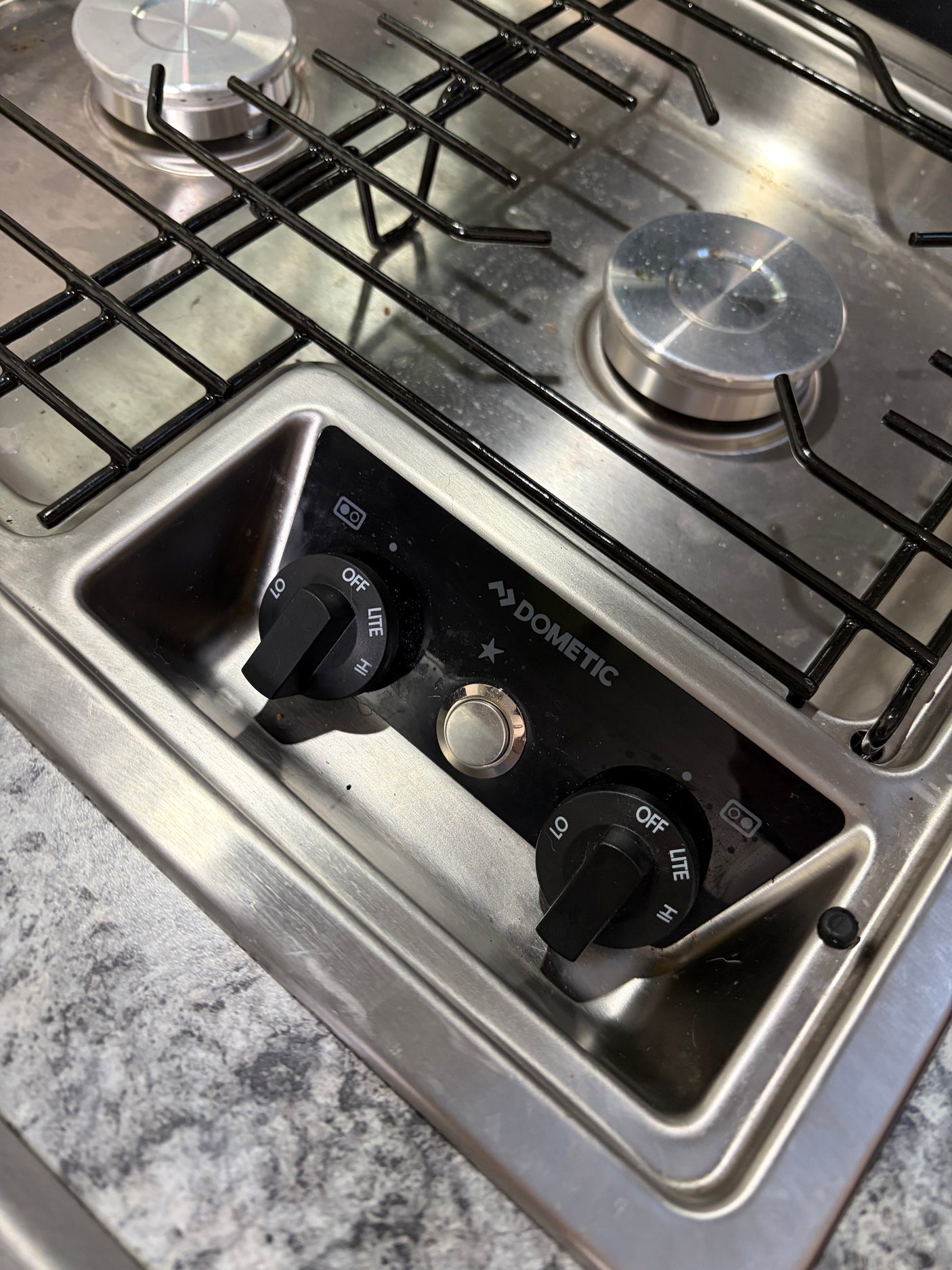 Stainless steel Dometic 2-burner RV rental stovetop with black grates, control knobs, and igniter button.