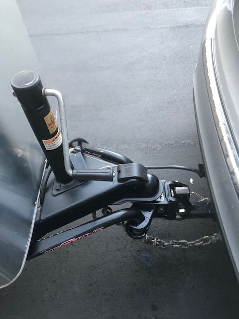 RV rental: Close-up of travel trailer hitch connected to tow vehicle, showing safety chains & jack. Ready for the road!