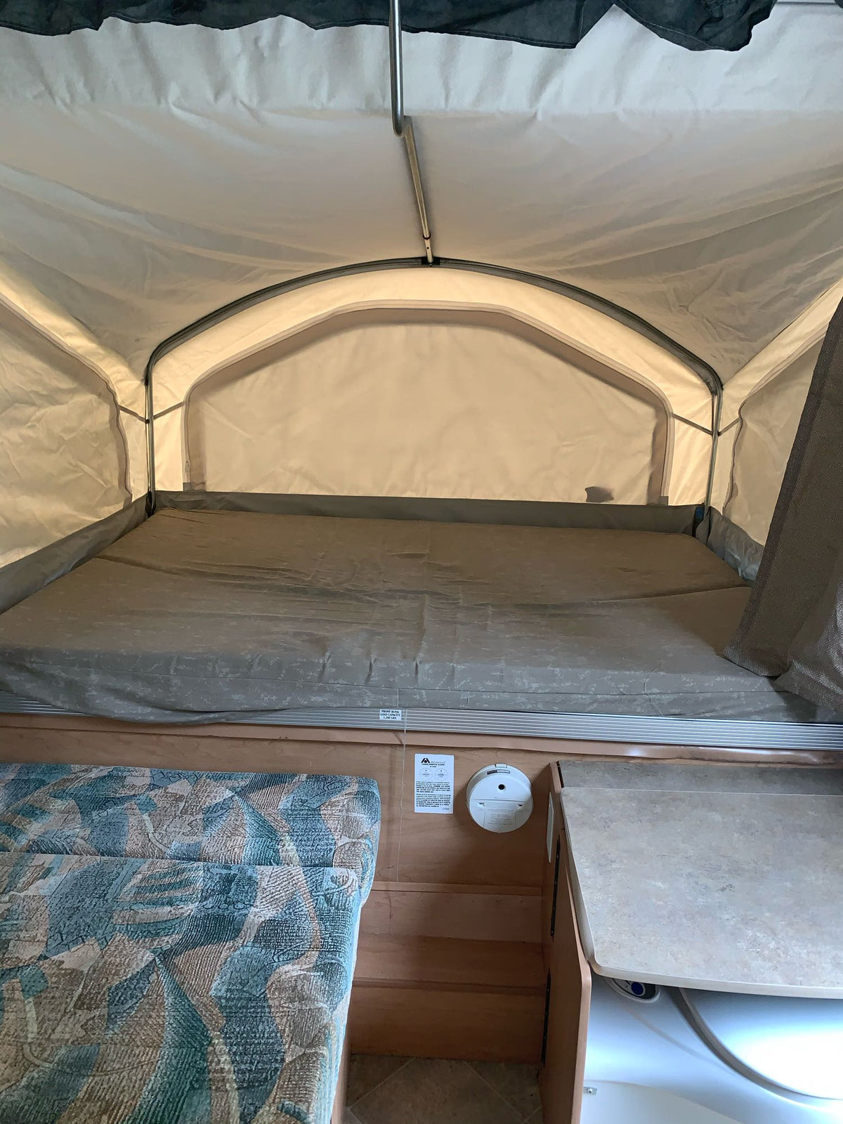 Inside a pop-up RV rental, featuring a spacious bed, light fabric walls, and a small built-in counter area. — photo 8