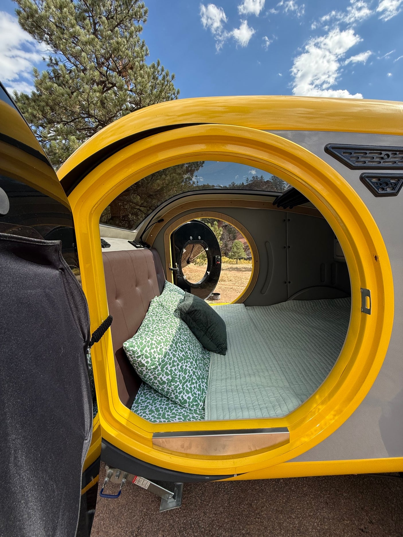 Cozy teardrop camper interior, perfect for an RV rental adventure. Bed with green pillows, open door to nature.