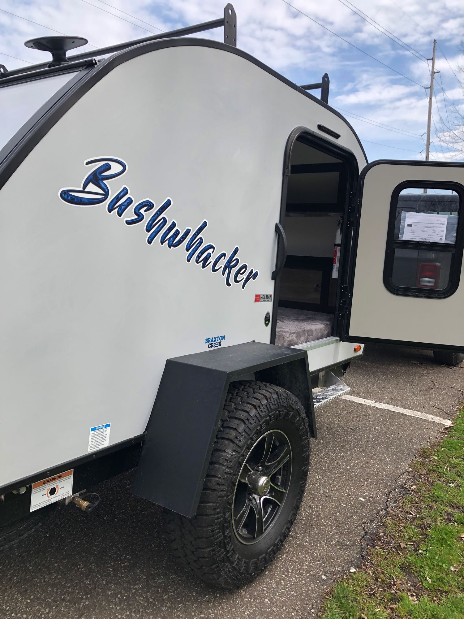 A Bushwhacker teardrop travel trailer for RV rental. Its side door is open, revealing a compact, bed-filled interior.