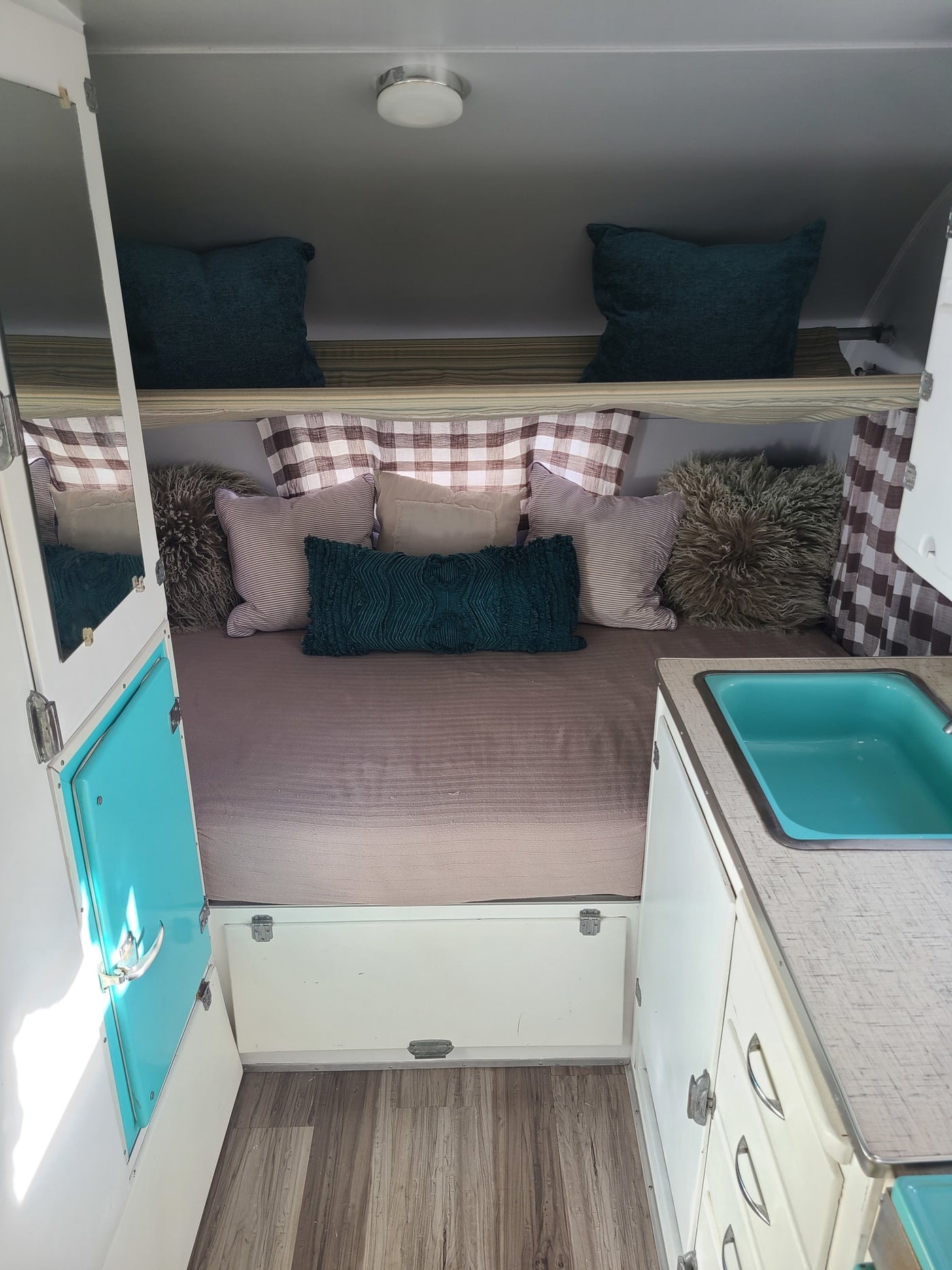 Cozy RV rental interior featuring a full bed with decorative pillows, bright teal sink, and plaid curtains. — photo 5