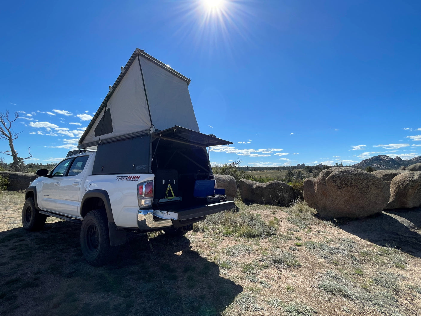 Explore nature with this RV rental! A white Toyota Tacoma truck with a raised rooftop tent & camp kitchen in rocky terrain.