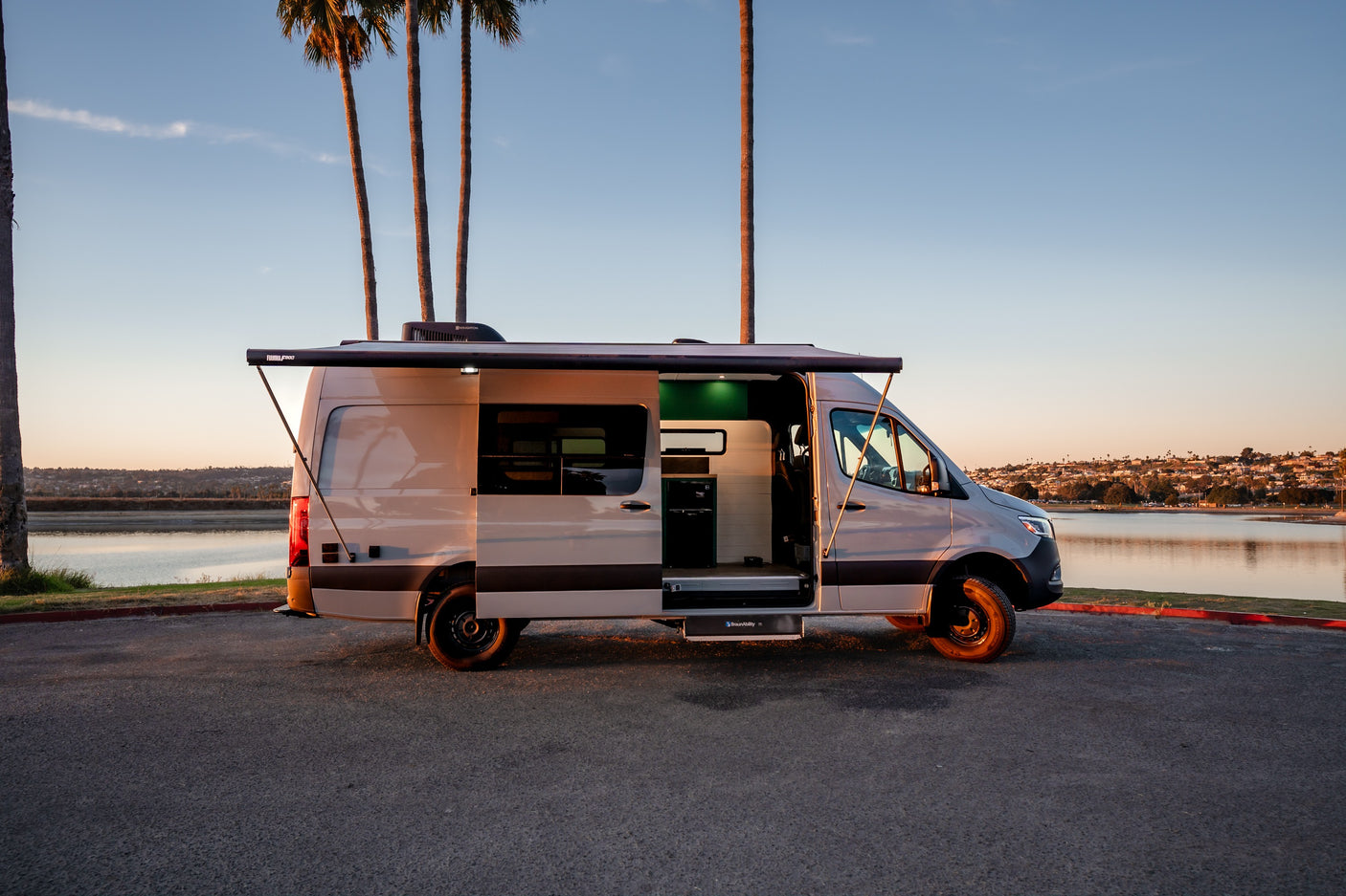 Experience comfort in this accessible rv rental camper van. Awning extended, door open, parked lakeside at golden hour.