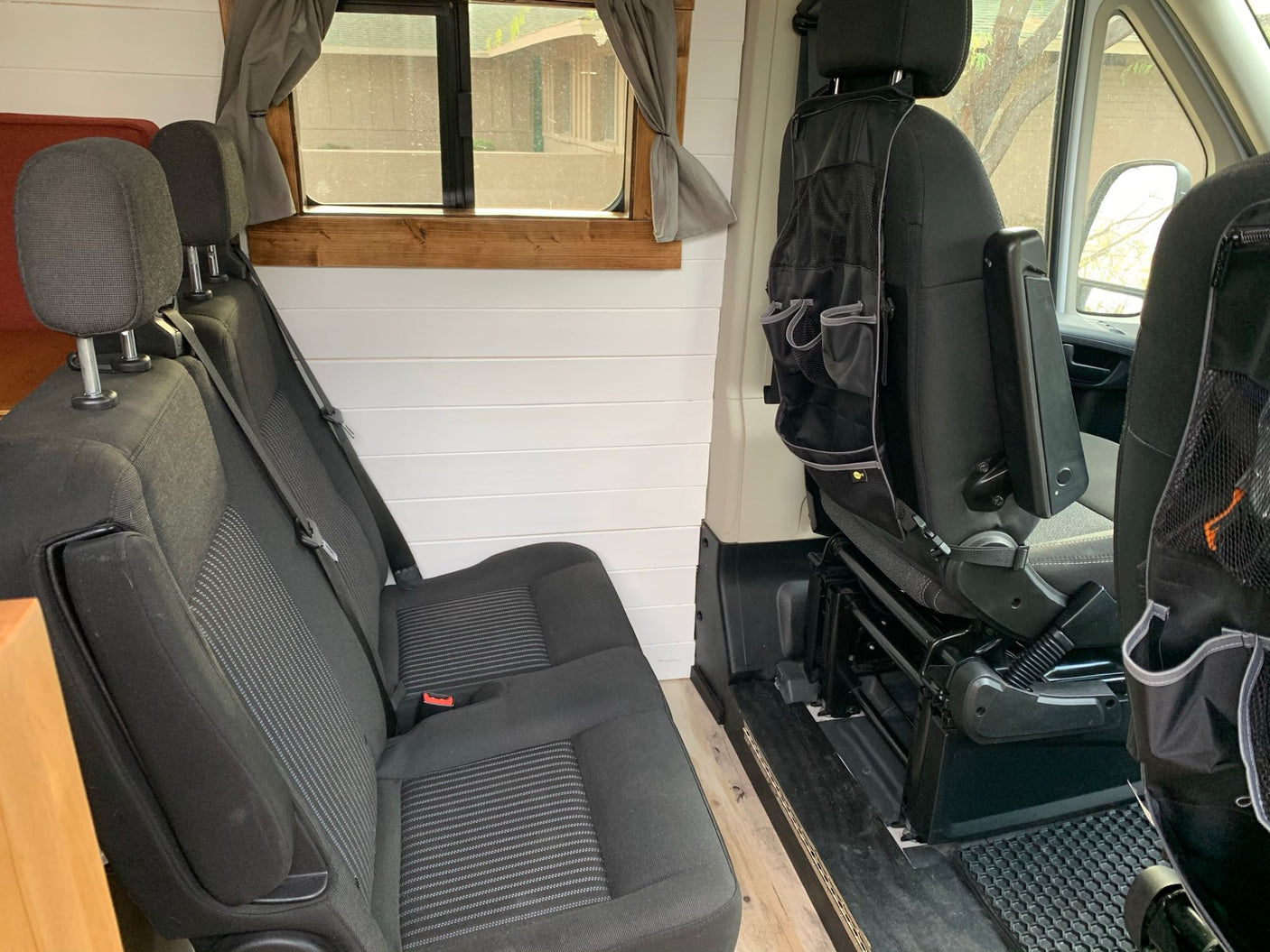 RV rental interior: custom white walls, wood window, rear bench seats, and front passenger seat with organizer.