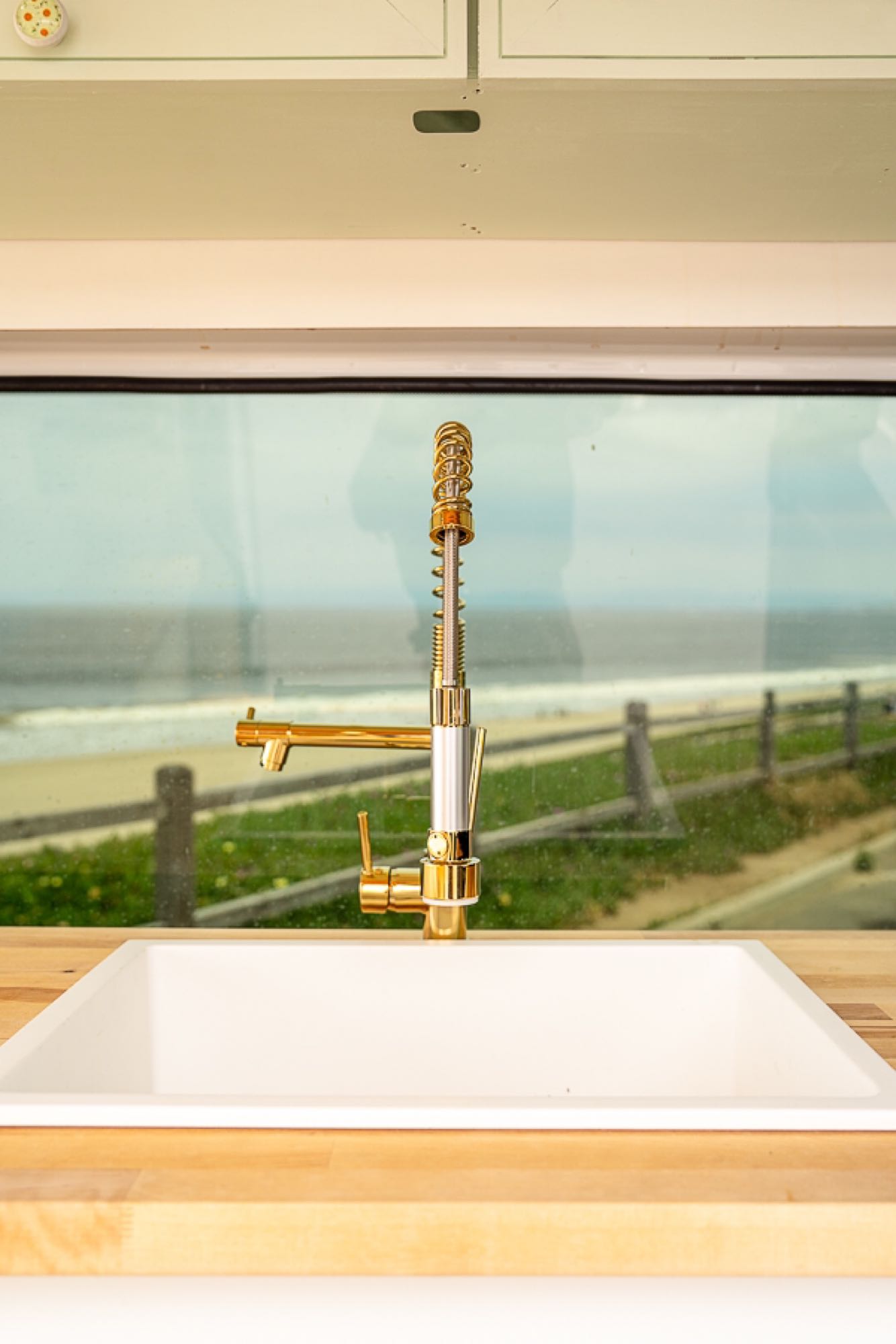 Modern RV rental kitchen with golden faucet, white sink, and panoramic ocean view. Perfect for travel adventures.