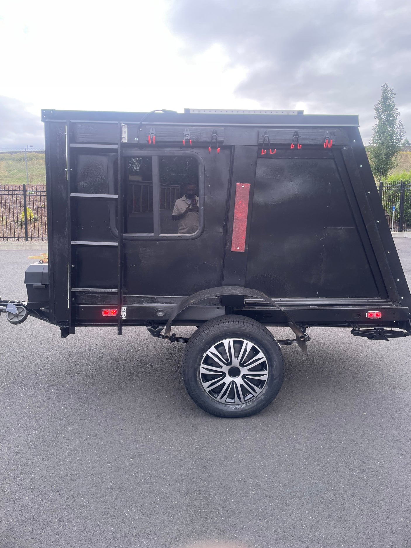 Explore with this compact black adventure trailer, perfect for RV rental. Features a window, wheel, and reflective accents.