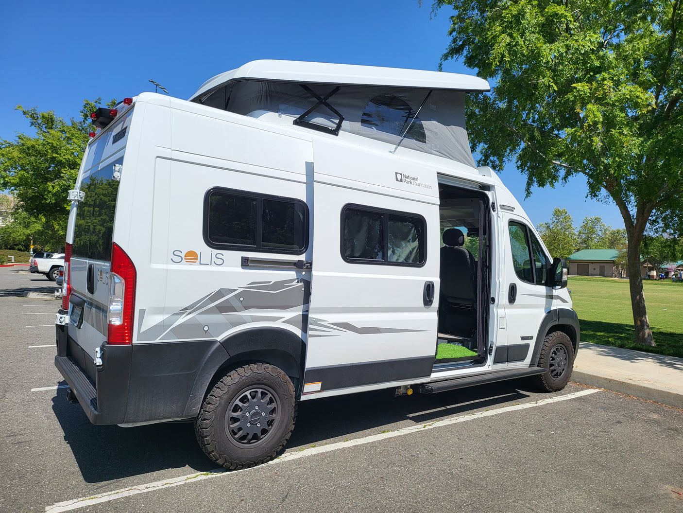 White Solis pop-top RV rental parked by a grassy park, ready for adventure.