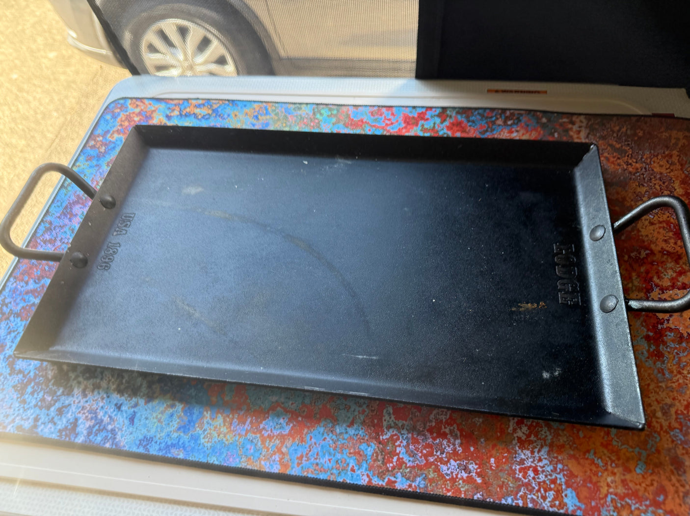 Lodge griddle on a vibrant mat, ready for cooking on your rv rental trip. View of RV window and tire.