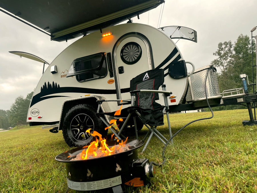 An RV rental teardrop camper with an awning extends over a cozy camp setup