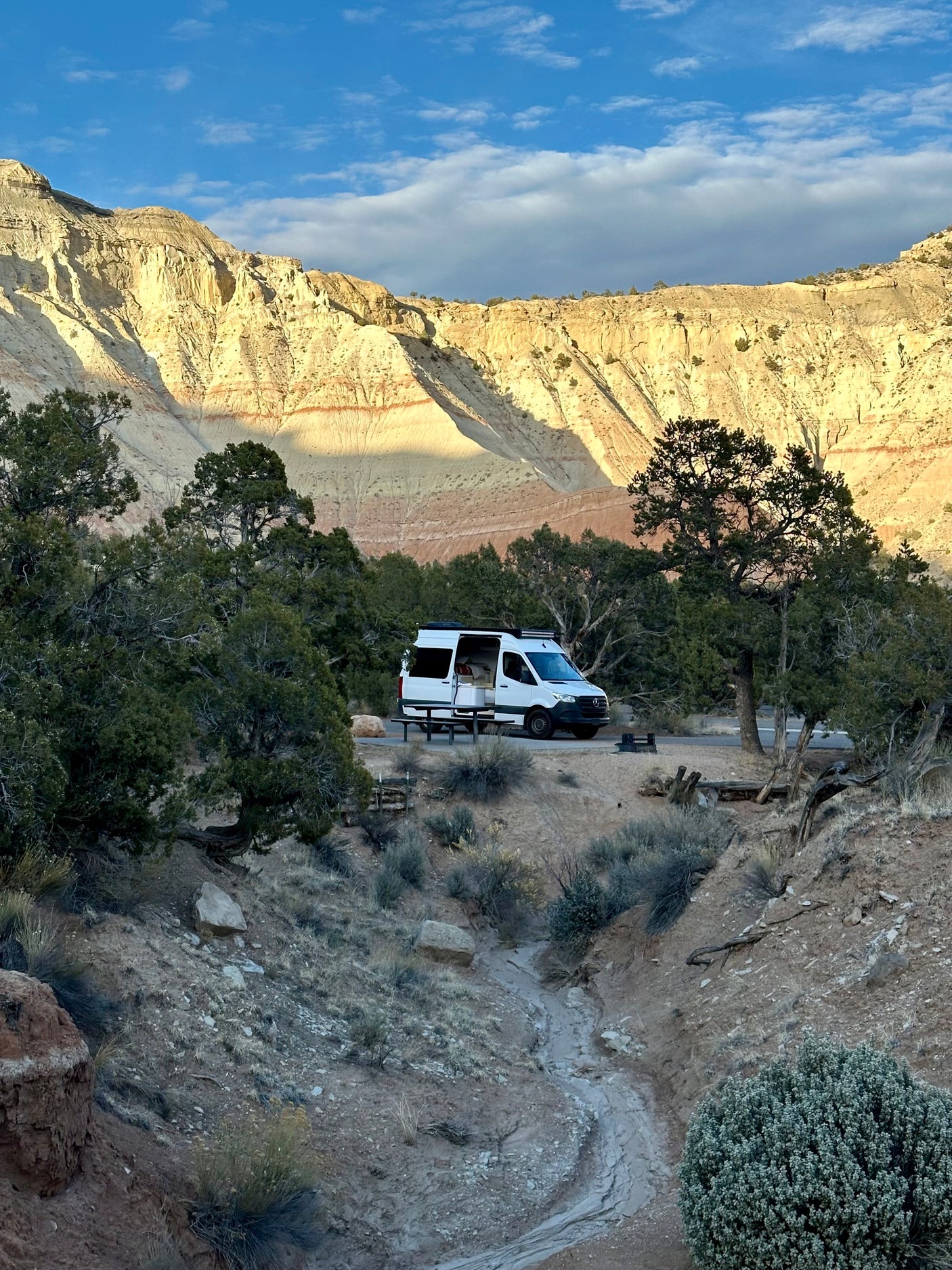 RV rental at a scenic desert campsite, nestled below towering mountains with distinctive striped rock formations under blue skies.
