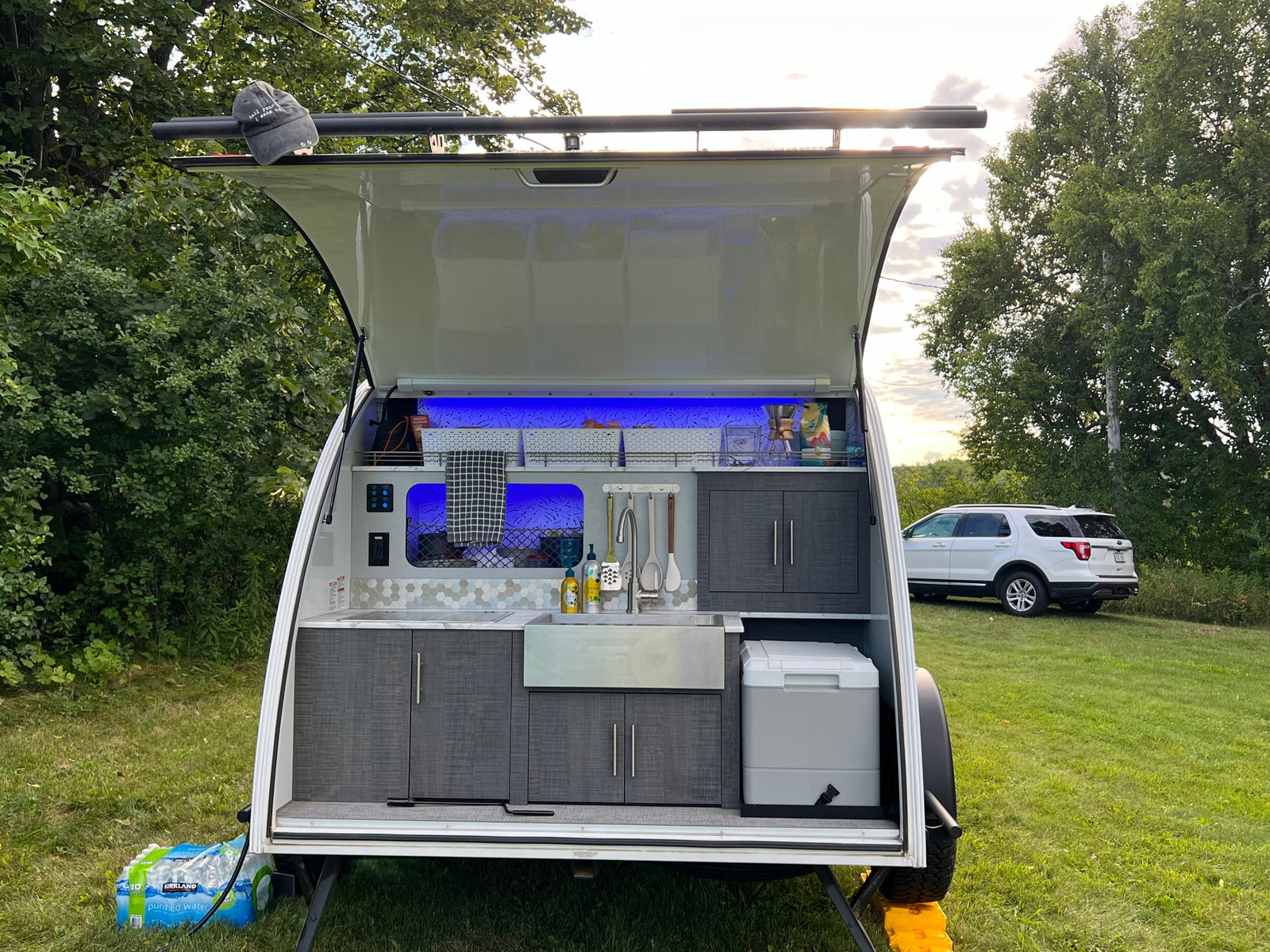 parked on grass. Perfect for outdoor camping with barns in background.|Close-up of a Luna Rover teardrop rv rental with black splatter graphics